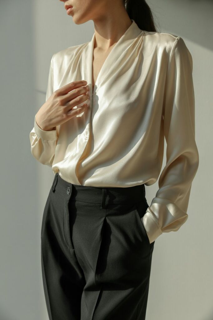 Cream silk flowy blouse tucked into high-waisted black trousers