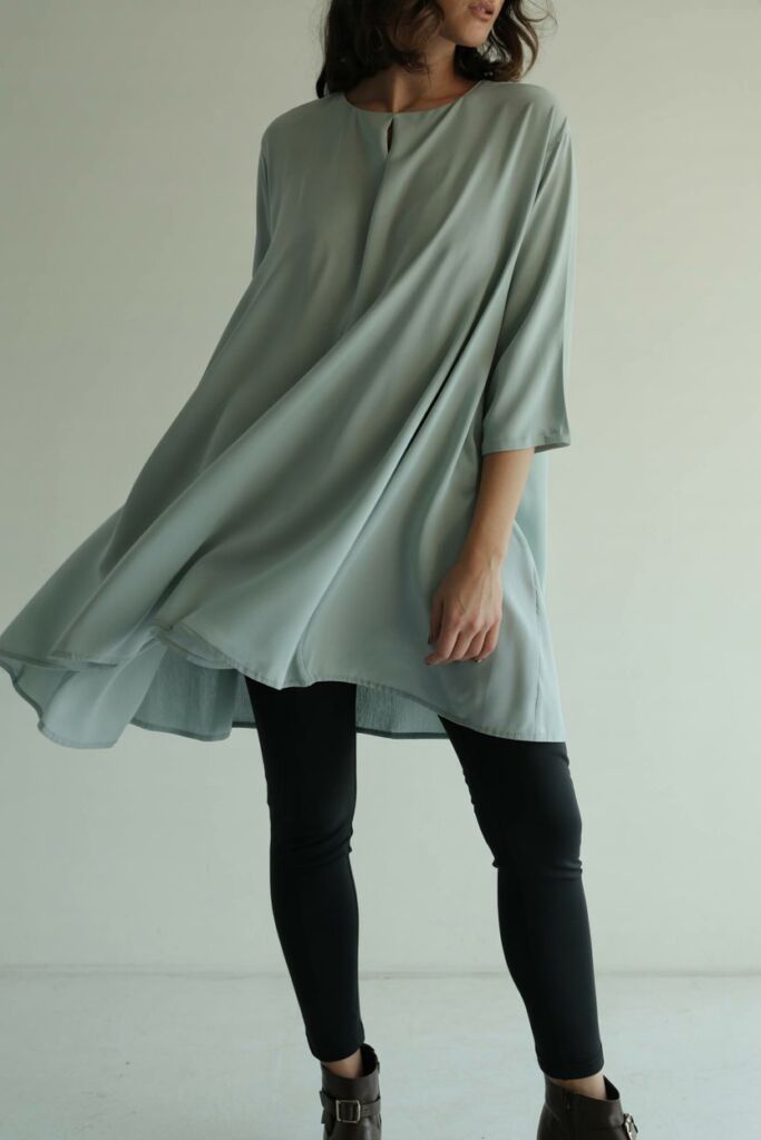 Flowy tunic blouse in solid color worn over black leggings and ankle boots