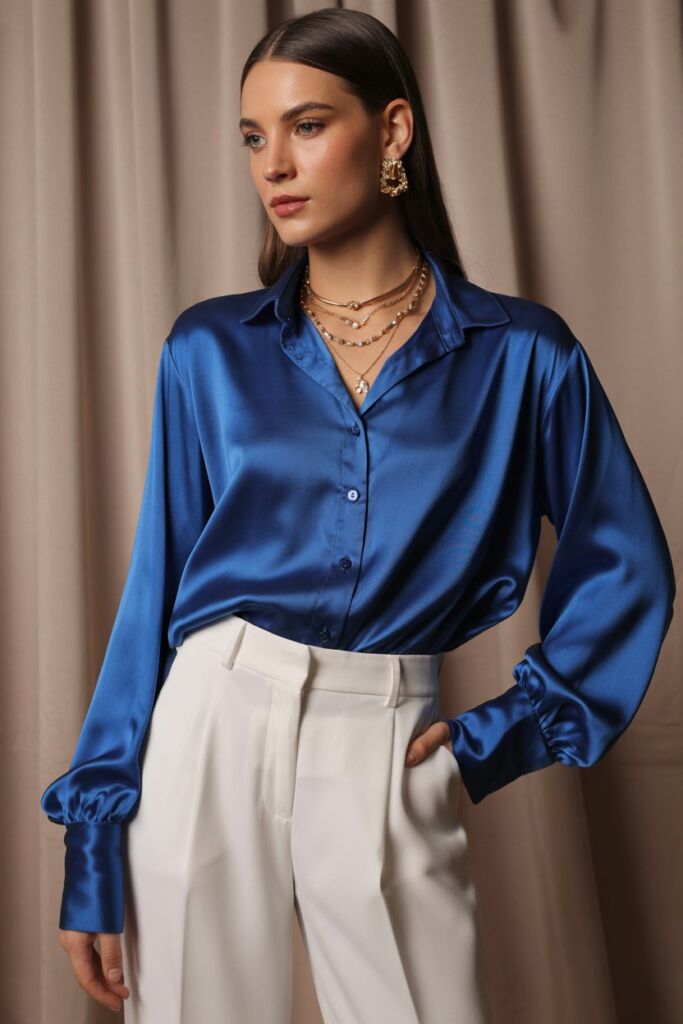 Model in silk royal blue blouse paired with white trousers and gold jewelry